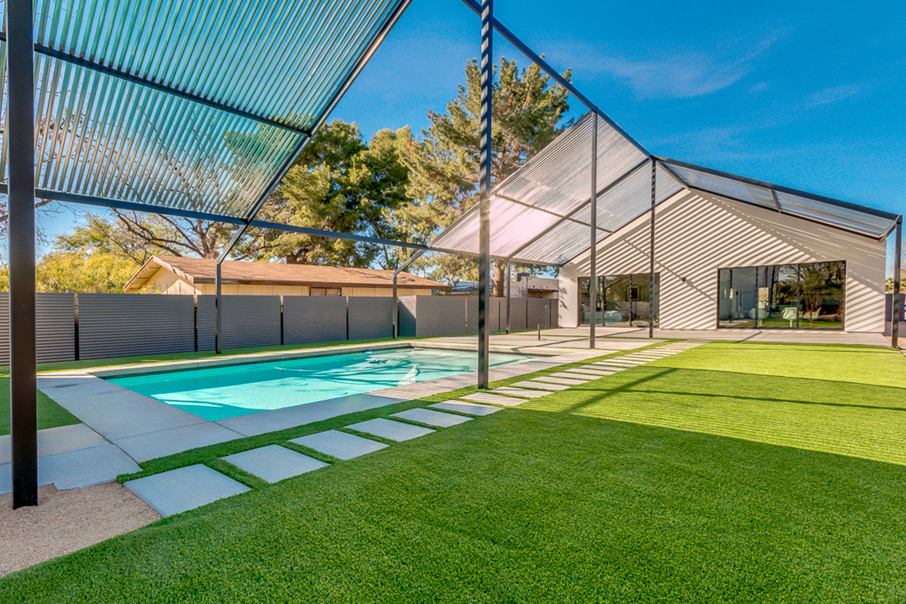 Phoenix home with expansive backyard that showcases a large pool surrounded with turf beneath a steel trellis